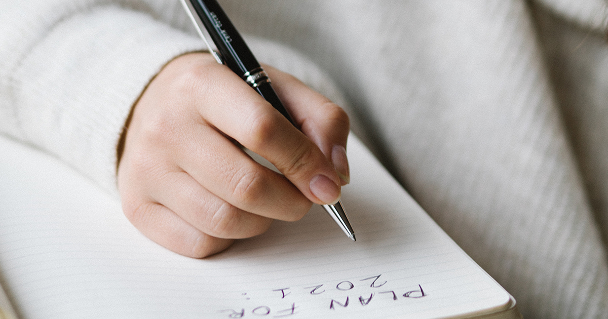 Woman's hand writing on a notebook planning for the new year.