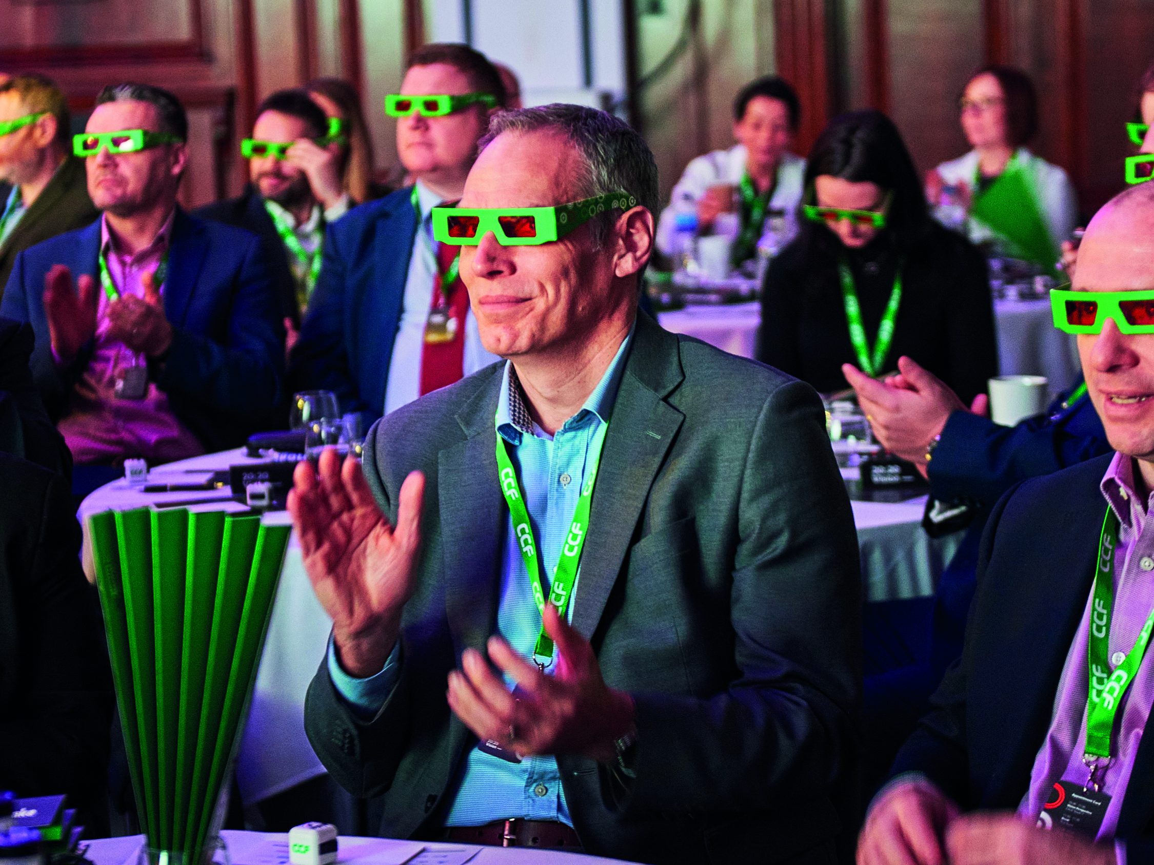 Still from a video of a client conference. People sitting around a table wearing green 3D glasses.