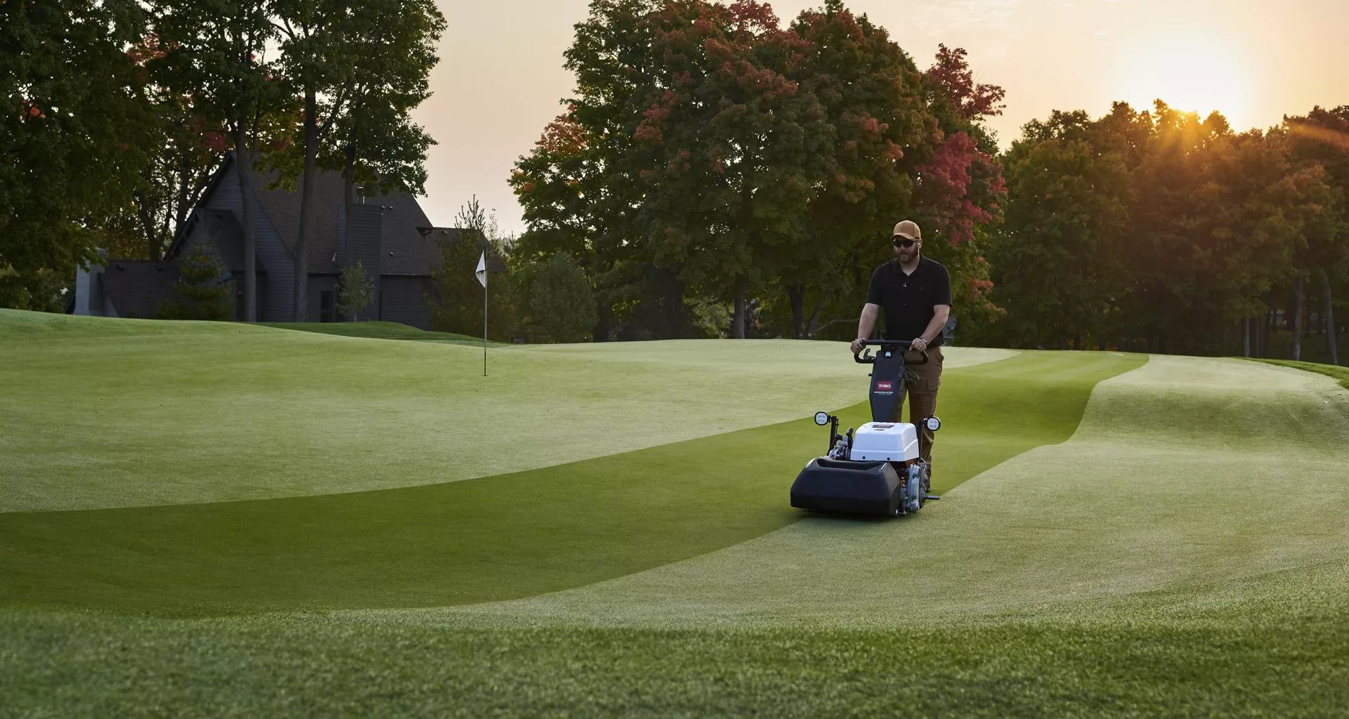 A man mowing a green space with a walk behind mower